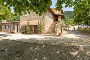A stone building with a staircase leading to a second floor, surrounded by potted plants and a gravel driveway. - Majestic Villa Retreat (Assisi)