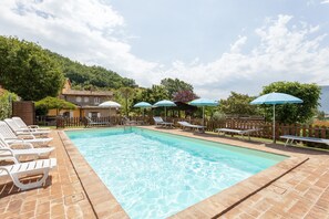 A swimming pool with lounge chairs and umbrellas, surrounded by a wooden fence and trees. - Majestic Villa Retreat (Assisi)