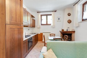 A compact kitchen with wooden cabinets, a stove, and a dining area with a table and chairs. - Majestic Villa Retreat (Assisi)