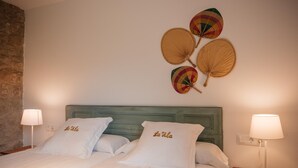 Ein Bett mit weißen Leinen und Kissen, ein Holzkopfschild und ein dekorativer Wandventilator.