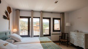 Ein Hotelzimmer mit zwei Betten, einem Schminktisch, einem Sessel und großen Fenstern mit Blick auf die Landschaft.