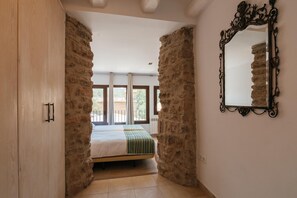 A bedroom with a bed, stone walls, a large mirror, and a view through a window. - Cottage in Castellnou With Forest Trails (Castellnou de Bages)