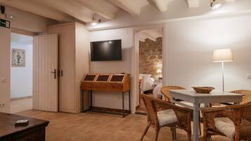 A room with a wooden table, wicker chairs, a flat-screen TV, and a stone wall.