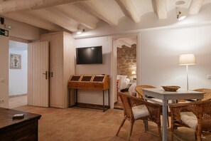 A room with a wooden table, wicker chairs, a flat-screen TV, and a stone wall.