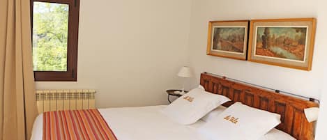Ein Hotelzimmer mit einem Bett, zwei Bildern an der Wand, einem Fenster mit Vorhängen, einem Nachttisch mit Lampe und einem Heizkörper.