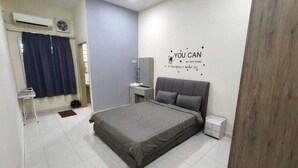 Quarto com cama, mesa de cabeceira, ar condicionado fixado na parede e ventilador de teto, além de uma frase motivacional na parede.