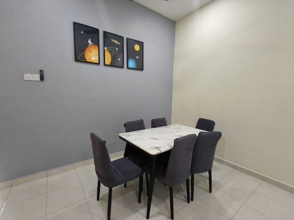 A dining area with a marble table and six chairs, a grey wall with three framed artworks, and a light switch.