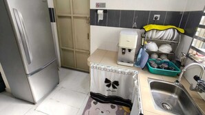 Uma cozinha compacta com geladeira, cafeteira, pia e um cesto de lixo com tampa.