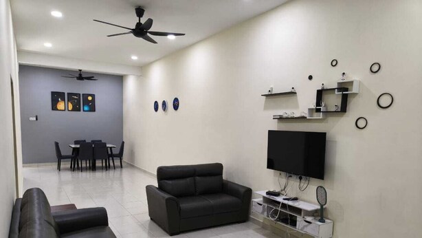 Uma sala de estar com um sofá, uma poltrona preta, uma TV e um ventilador de teto.