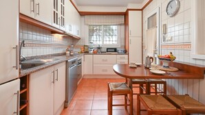 Een keuken met witte kastjes, een magnetron, een spoelbak en een eethoek met een tafel en stoelen.