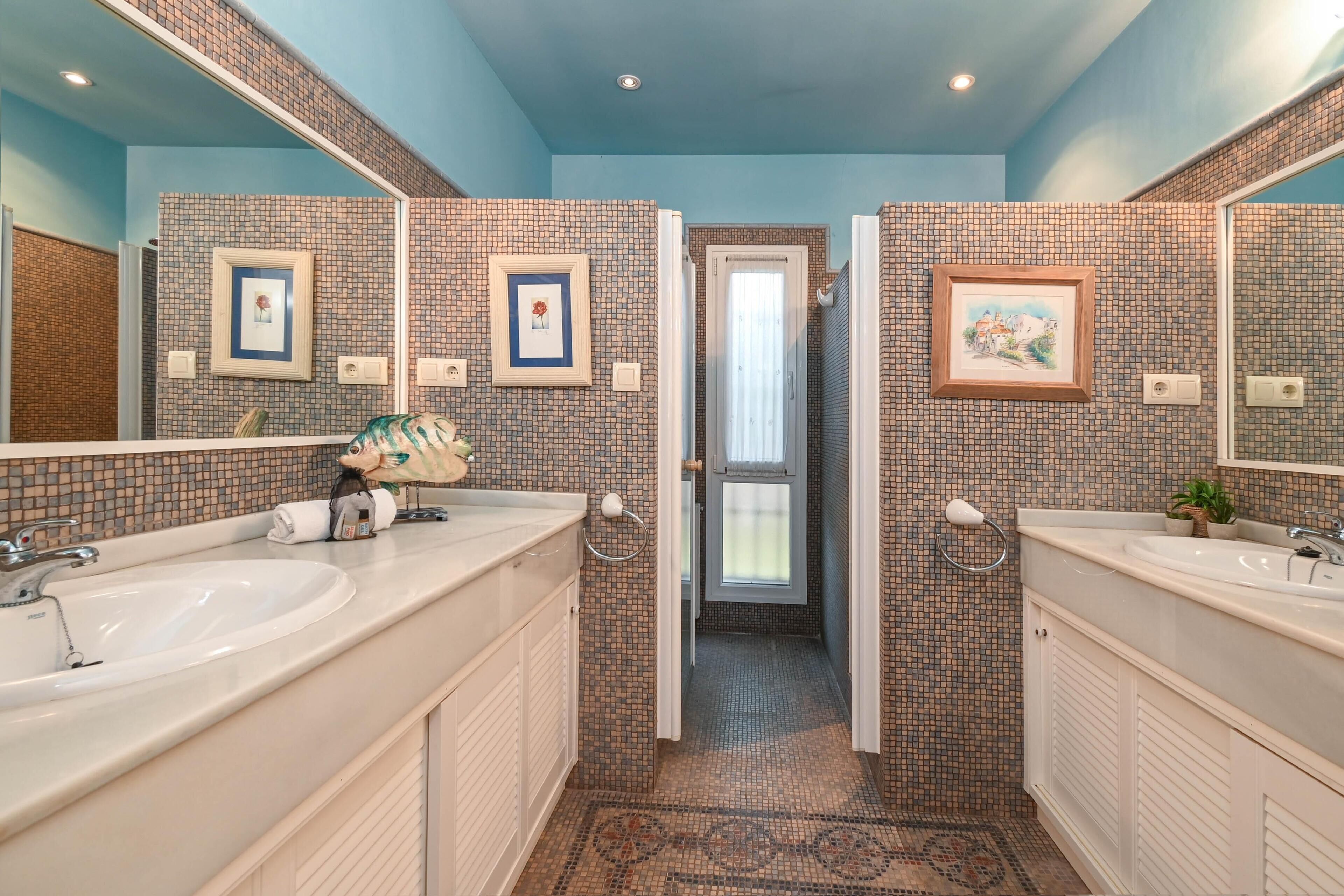 A bathroom with two sinks, tiled walls, framed pictures, and a patterned floor.