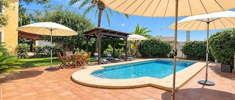Piscina con sillas de descanso y sombrillas, rodeada de un jardín y un edificio.