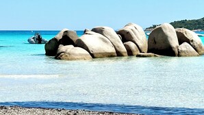 Une plage dégagée avec de gros rochers dans l’eau et un bateau en arrière-plan.