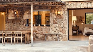 Un bâtiment en pierre avec un toit en tuiles, une table et des chaises en bois à l’extérieur, et une vue sur l’intérieur.