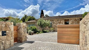 A stone-walled building with a tiled roof, a wooden gate, and a cobblestone driveway. - Villa 8 persons Heated swimming pool. Petanque court Electric car terminal (Porto-Vecchio)