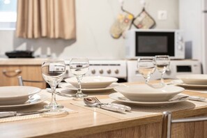 Una mesa de comedor dispuesta con platos, vasos y cubiertos, con un microondas y un horno al fondo.