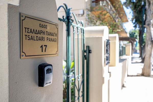 Une entrée d’immeuble avec une plaque indiquant « TZALDARI PANAGI 17 » et un clavier de sécurité.