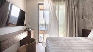 A modern hotel room with a large bed, a flat-screen TV, a desk, and a view of the outdoors. - Infinity Rise Villa, a Distinctive Private Stay (Agia Pelagia)