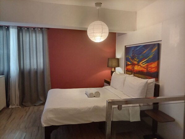 Una camera d'albergo con un letto, un comodino, una lampada, un quadro e vista sul cielo.