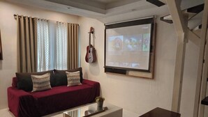 Un soggiorno con un divano rosso, un tavolino da caffè, una TV a parete e una chitarra.