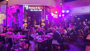 Un ristorante con insegna al neon, tavoli, sedie e clienti che cenano.