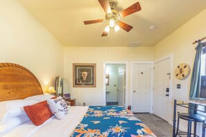 Quarto com cama, ventilador de teto, porta, espelho e relógio na parede.