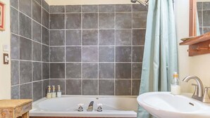 A bathroom with a bathtub, a sink, and a wooden stool. - Buffalo Spirit - Stardust Inn - Triple Z (Medicine Park)