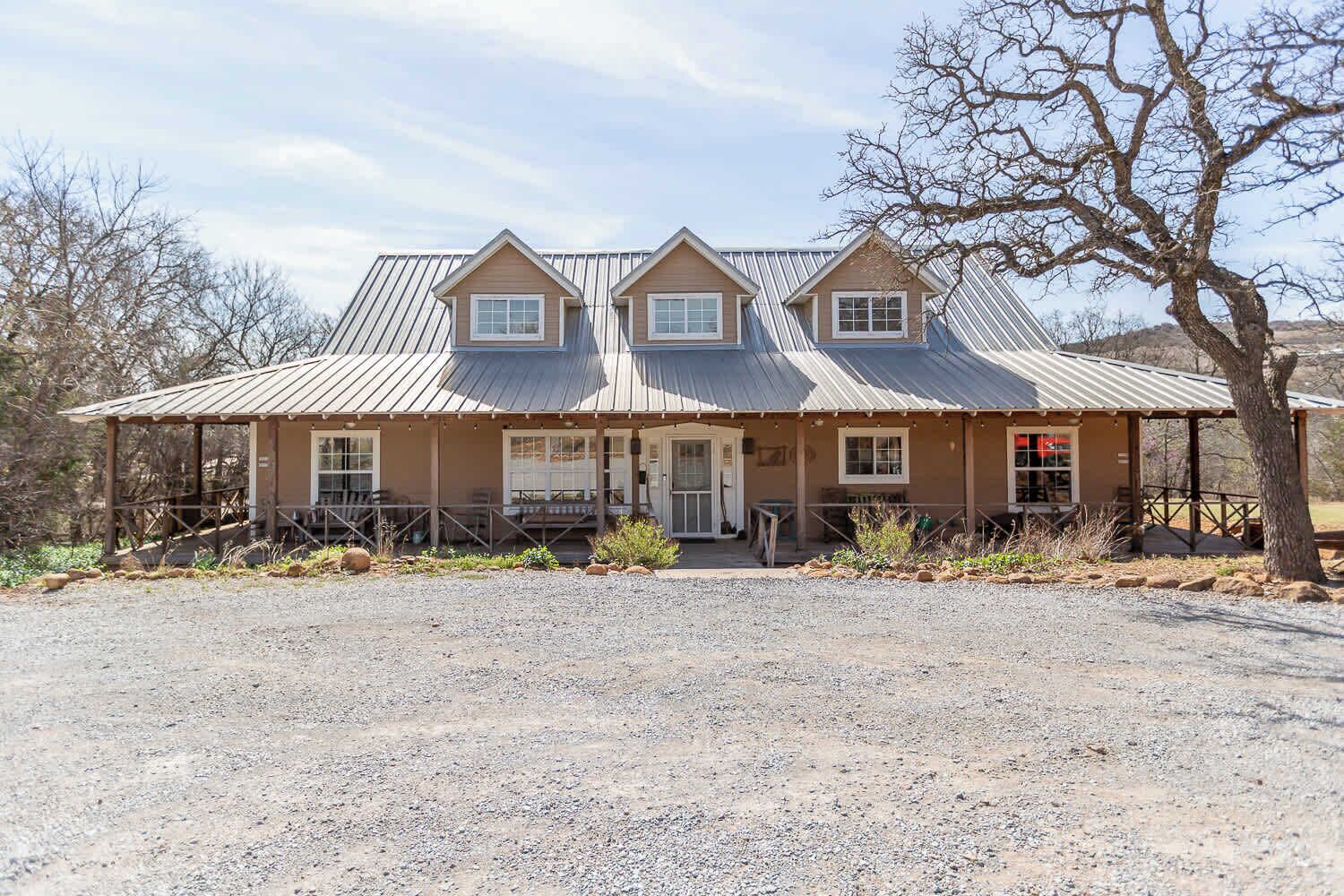 A two-story building with a metal roof, a porch with chairs, and a gravel driveway.