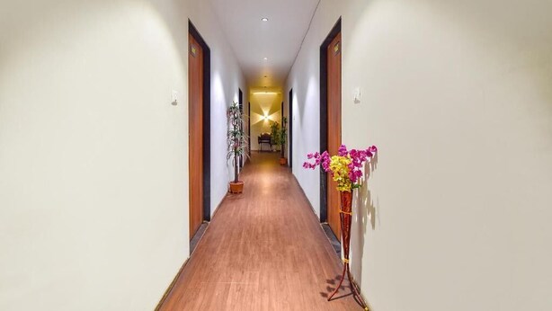 A hotel hallway with wooden flooring, a central light fixture, and a potted plant on the right. - HOTEL NIDHIVAN   (Surat)