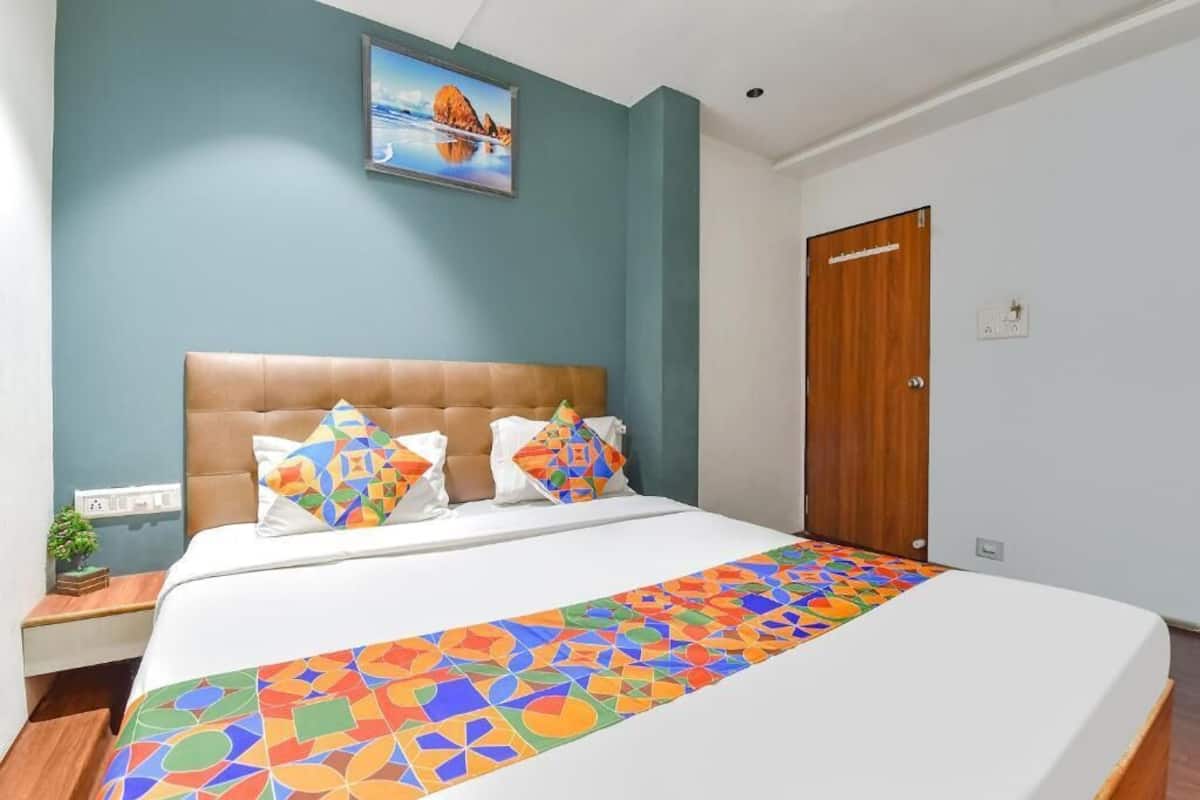 A bedroom with a large bed, a headboard, a nightstand, a wall-mounted painting, and a wooden door.