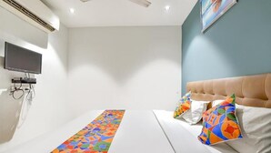 A hotel room with a bed, a TV, and a wall-mounted air conditioner. - HOTEL NIDHIVAN   (Surat)