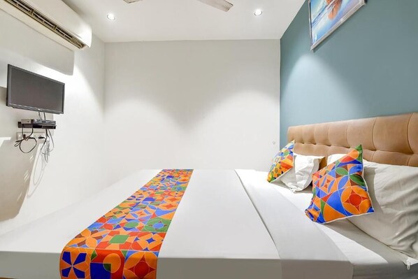 A hotel room with a bed, a TV, and a wall-mounted air conditioner.