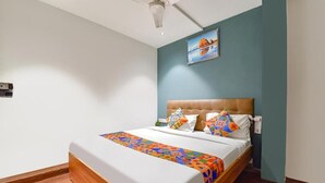 A bedroom with a bed, a ceiling fan, a painting on the wall, and a wooden floor. - HOTEL NIDHIVAN   (Surat)