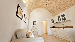 Una sala de estar con un sofá, una cocina con armarios blancos y techo de piedra.