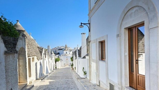 Una estrecha calle adoquinada flanqueada por edificios blancos, una puerta de madera y un farol.