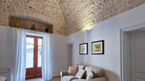 Una habitación con techo de piedra, una puerta de madera, un sofá color crema y dos cuadros en la pared.