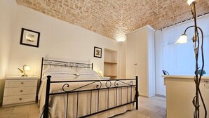 Un dormitorio con estructura de cama metálica, mesitas de noche con lámparas, un armario y vistas a través de una ventana.