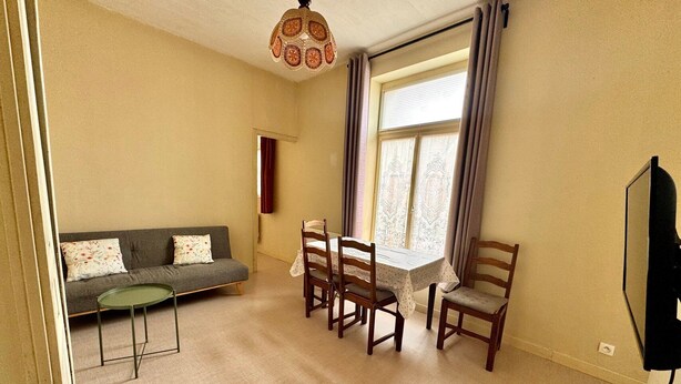 Een woonkamer met een bank, eettafel, stoelen, een plafondlamp met een patroon en een raam met gordijnen.