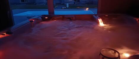 Un jacuzzi avec une télécommande, de la vapeur qui s’élève et une vue sur les maisons à travers une fenêtre.