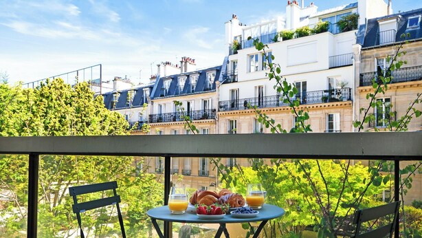 Un balcon avec une table dressée pour le petit-déjeuner, donnant sur une rangée de bâtiments de style européen.