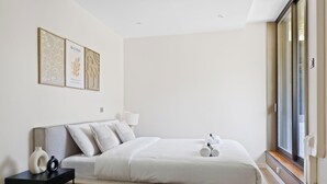 Une chambre à coucher au style minimaliste, avec un lit, une table de chevet, une lampe et une œuvre d’art accrochée au mur.