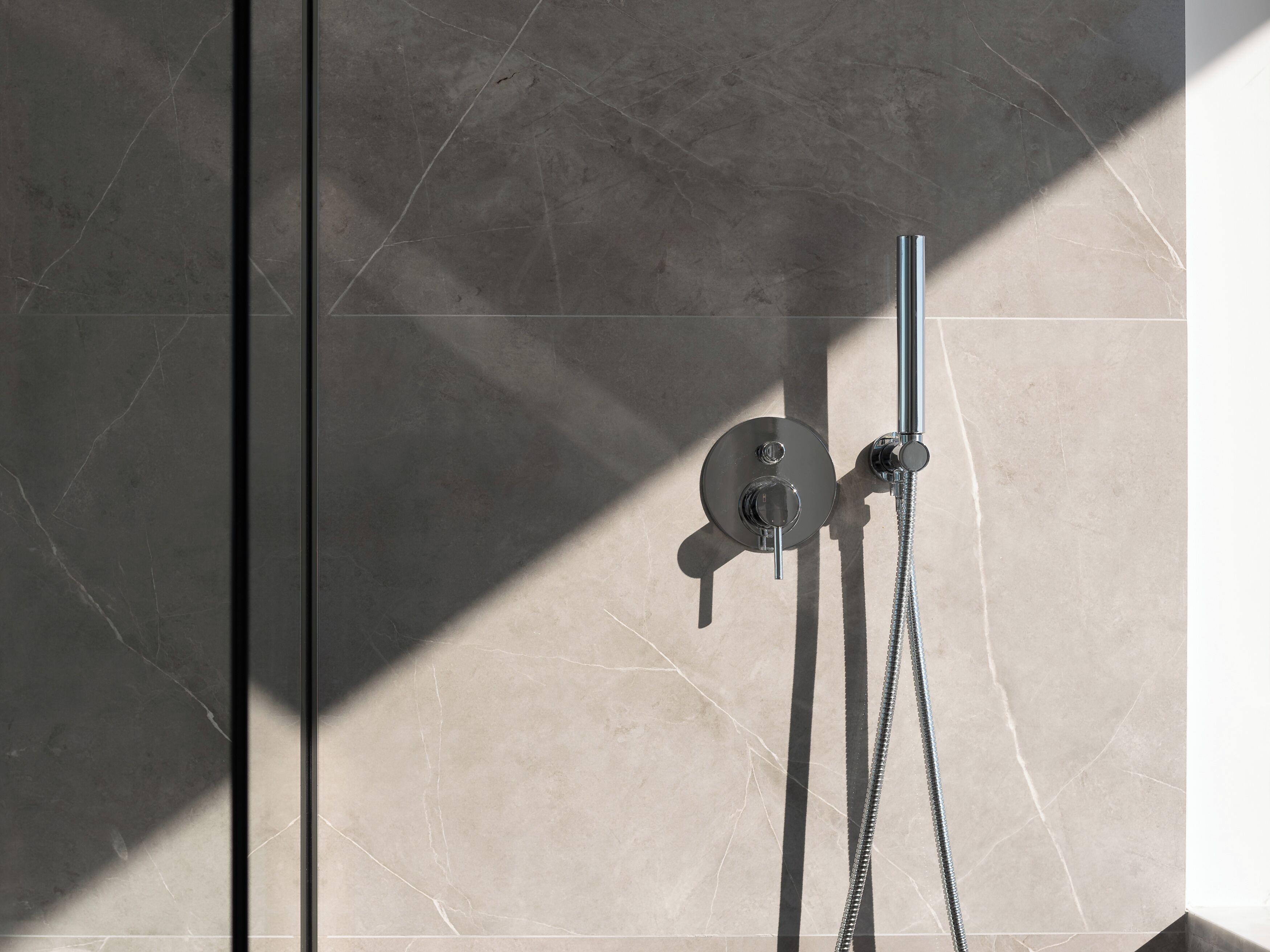 A shower with a chrome faucet and hose, set against a tiled wall with a geometric pattern.