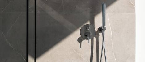 A shower with a chrome faucet and hose, set against a tiled wall with a geometric pattern.