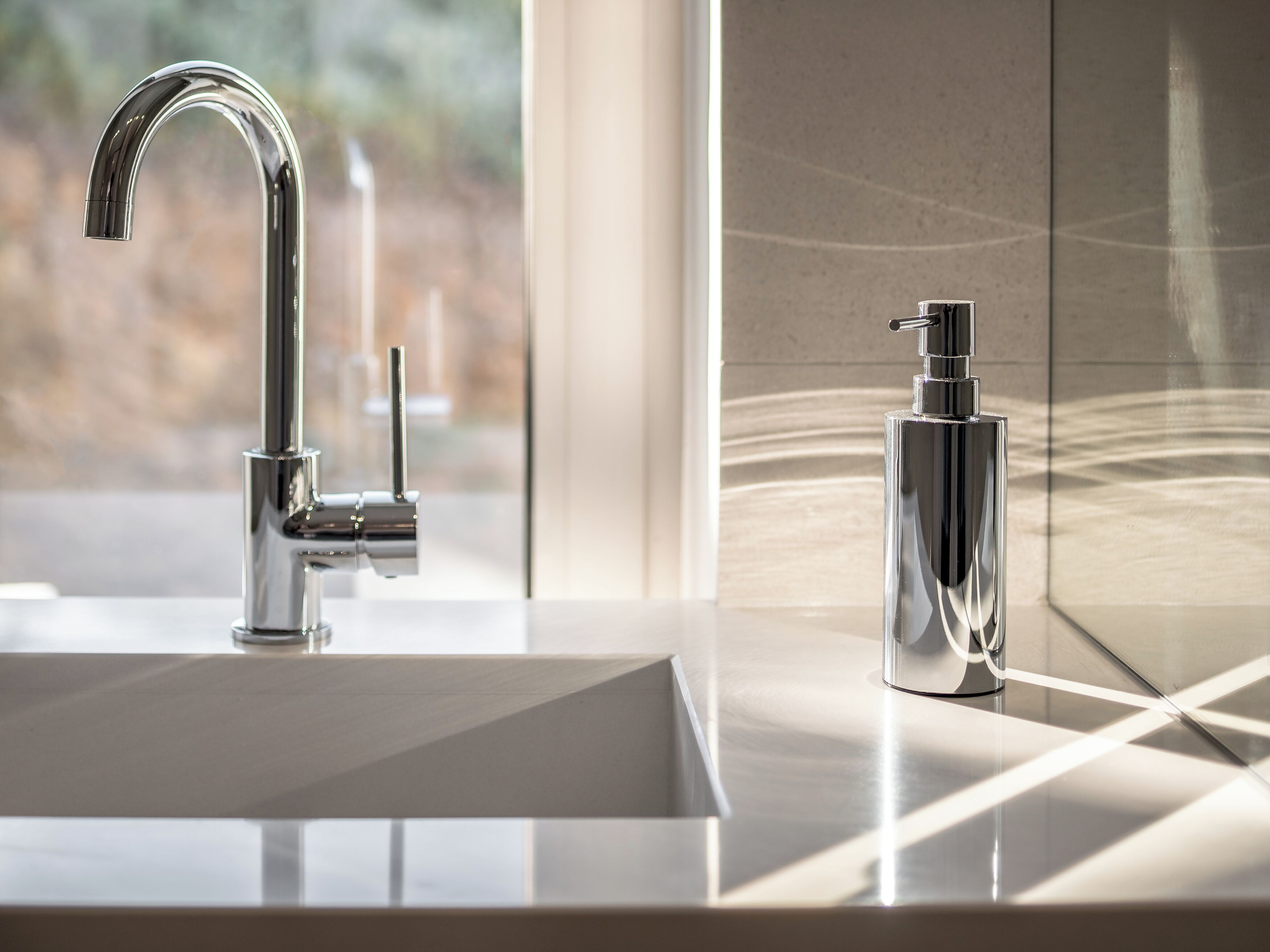 Un baño moderno con un grifo cromado, dispensador de jabón y un ventanal grande.