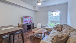Un salon avec un plancher en bois, un canapé, une table basse, un téléviseur et une fenêtre.