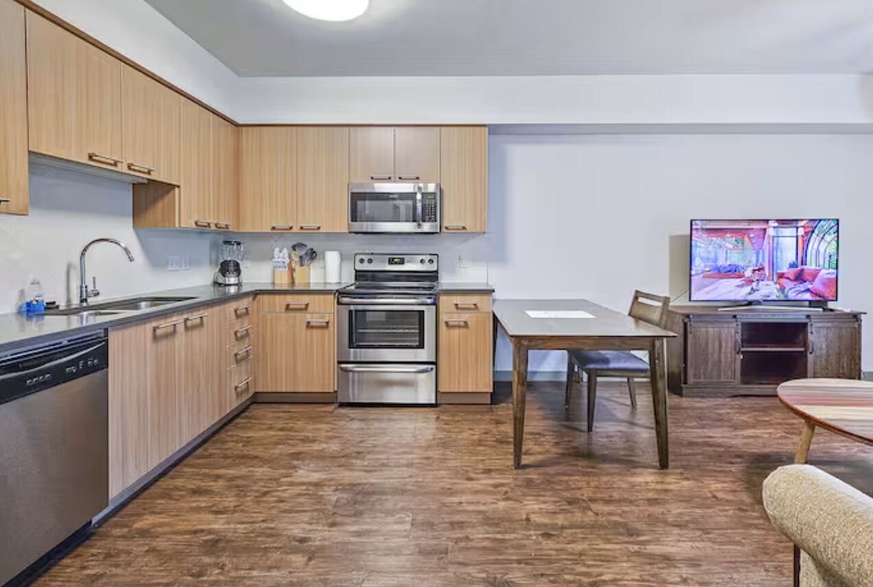 A modern kitchen with wooden cabinets, stainless steel appliances, and a dining area with a table and chairs.