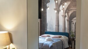 A bedroom with a bed, pillows, a bedside table with a plant, and a wall with a cityscape mural. - Elegant apartment in the heart of Vigevano, a stone's throw from Piazza Ducale (Vigevano)