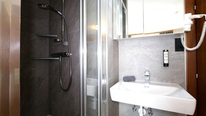 Un baño moderno con ducha envuelta en cristal, un lavabo blanco y un espejo sobre él.