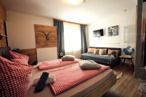 Un dormitorio con cama, sofá, cabecera de madera, una obra de arte en la pared y una ventana con cortinas.