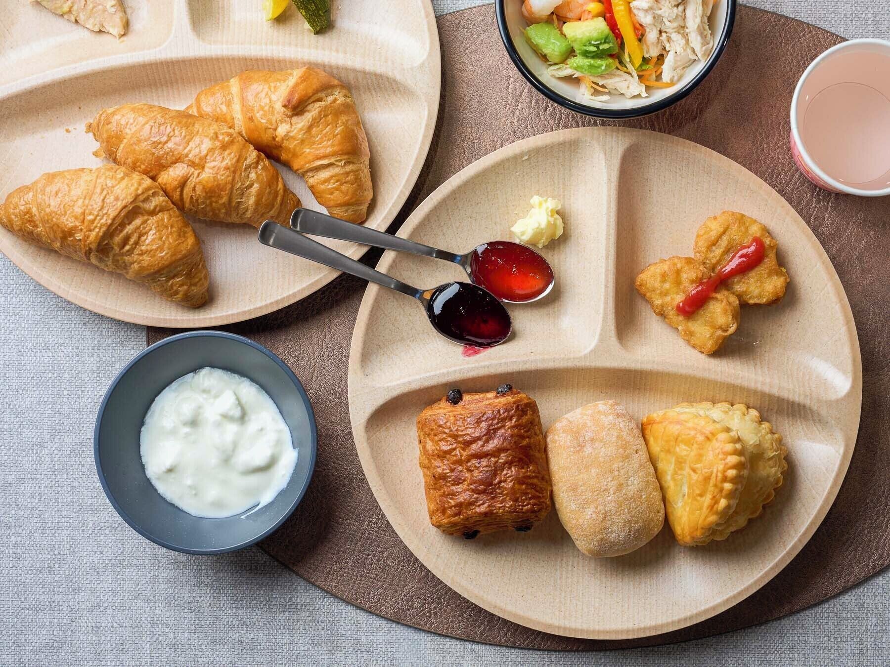 A meal with croissants, a bowl of yogurt, and a plate with various pastries.